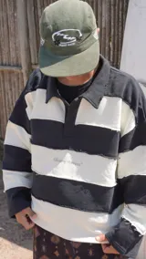 Buzo estilo rugby de corte oversize, con diseño de rayas horizontales anchas en blanco y negro. Presenta cuello tipo polo, costuras expuestas con efecto desflecado y el logo de la marca estampado en el pecho.