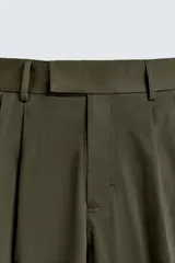 Pantalón negro de corte relaxed fit y estilo wide leg, con pliegues frontales dobles, bolsillos delanteros y detalle de bolsillos traseros de vivo. Cierre frontal cruzado con cremallera y gancho metálico oculto.