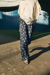 Pantalón de tiro medio con cintura elástica y bolsillos ocultos en costura. Presenta un diseño de corte recto con dobladillo ancho en el bajo y un estampado geométrico sobre fondo oscuro.