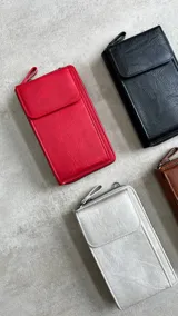 Cartera portacelular con correa larga, cierre con cremallera y solapa con broche imantado.