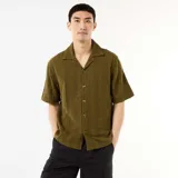 Camisa de manga corta color verde militar, con cuello solapa y cierre frontal de botones. Confeccionada en punto fantasía de algodón con sutiles rayas verticales texturizadas.