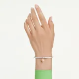 Brazalete rígido de la colección Idyllia, con diseño de media caña adornado con cristales transparentes. Presenta un dije central en forma de corazón tipo medallón, con baño en tono oro y una zirconia rosa en una cara, y pavé de cristales con baño de rodio en la otra.