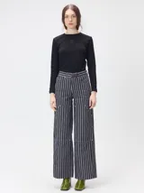 Pantalón de tiro medio y pierna ancha confeccionado en denim de algodón grueso. Presenta un diseño a rayas verticales en tonos azul y celeste, con costuras en contraste color rojo, bolsillos laterales tipo cargo y remaches metálicos.