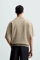 Polo de punto color verde oliva, de manga corta y corte relajado. Presenta cuello solapa con cierre frontal de cremallera.