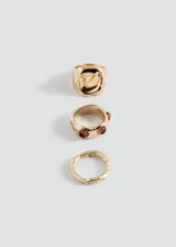 Set de tres anillos dorados de diseño irregular. Incluye un anillo ancho con forma orgánica, un anillo mediano incrustado con piedras marrones y un anillo fino con textura grabada.