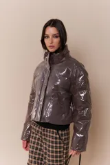 Campera puffer corta color marrón con acabado vinílico brillante, cuello alto y cierre frontal con broches a presión.