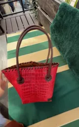 Cartera de cuero con textura crocco en color rojo, de silueta estructurada, manijas largas marrones y detalles de terminación artesanal en el borde superior.