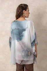 Blusa tipo túnica de gasa semitransparente con escote en V y mangas amplias. Presenta un diseño estampado con efecto acuarela en tonos azules, grises y marrones sobre fondo blanco.