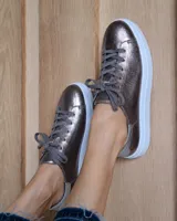 Zapatilla urbana de cuero metalizado en tono bronce, con cordones al tono y suela de plataforma blanca.