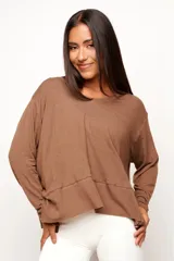 Remera de manga larga color marrón, confeccionada en una mezcla de viscosa, lino y elastano. Presenta un corte relajado con diseño asimétrico, destacando una costura horizontal en la parte frontal y bordes sin remate que le otorgan un estilo descontracturado.