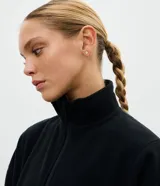 Buzo deportivo de fleece color crema, con cuello alto y cierre frontal parcial. Presenta mangas largas con puños elásticos y un diseño holgado con recortes frontales.