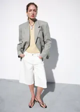 Bermuda de denim blanca con diseño recto y tiro medio, de estilo vaquero con cinco bolsillos, trabillas y cierre frontal con botón y cremallera.