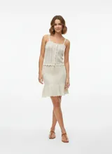 Pollera corta tejida en punto calado, color beige, con tiro medio, cintura elástica con cordón ajustable y ruedo con volado.