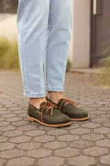 Zapatos náuticos de cuero verde oscuro, estilo mocasín con cordones de cuero marrón claro, costuras visibles en contraste y suela plana.