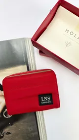 Billetera corta de diseño capitoneado con cierre perimetral y solapa frontal. Cuenta con compartimentos internos para tarjetas y billetes, e incluye una correa de mano desmontable.