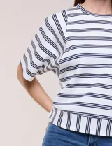 Remera de corte holgado color blanco con rayas horizontales oscuras, escote redondo a la base y mangas cortas amplias tipo murciélago. Presenta una banda ancha en el ruedo inferior con rayas verticales.