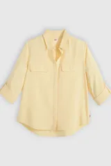 Camisa de lino color amarillo pastel, con bolsillos frontales con solapa, mangas largas remangadas y cierre frontal con botones.
