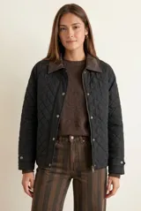 Campera negra de diseño capitoneado con cuello de solapa en contraste color marrón. Presenta cierre frontal con cremallera y botones a presión, mangas largas con puños ajustables y un corte recto.