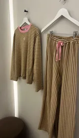 Pijama set de dos piezas compuesto por una remera de manga larga a rayas horizontales con cuello redondo celeste, y un pantalón largo de corte holgado a rayas verticales con cordón de ajuste en la cintura.