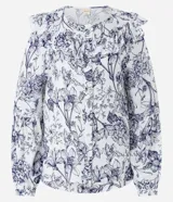 Blusa blanca estampada con flores azules, de mangas largas abullonadas con puños ajustados y volado en el cuello.