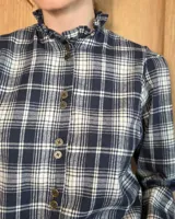 Camisa de algodón con estampado de rayas verticales finas, cuello alto con volados, cierre frontal con botones dobles y mangas largas con puños elásticos terminados en volados.