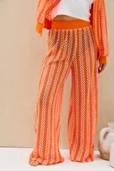 Conjunto de dos piezas tejido a crochet con diseño de ondas en tonos naranja, rosado y amarillo, compuesto por una camisa de manga larga y un pantalón largo de corte recto.