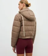 Campera puffer deportiva Get Over, color blanco con detalles de bies en color negro a lo largo de las mangas. Presenta cuello alto con capucha integrada, cierre frontal con botones a presión, bolsillos laterales con cremallera y puños con elásticos.