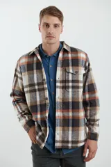 Sobrecamisa de hombre con diseño a cuadros en tonos marrón, beige y blanco. Confeccionada en tejido peludito suave, con cuello clásico, cierre frontal con botones, bolsillo superior y mangas largas con puños abotonados.