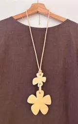 Collar largo con cordón ajustable color beige y dos dijes de flores de acrílico marmoleado color crema.