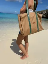 Bolso tipo tote bag de lona color beige, con asas de cuero verde.