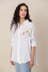 Camisa blanca de lino de corte oversize, con mangas largas y detalle de bordado colorido en el pecho.