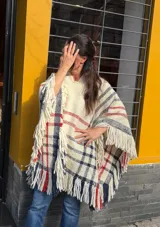 Poncho de lana merino tejido en telar de peine, color marfil con diseño a cuadros en tonos azul marino y rojo, terminado con flecos en el ruedo.