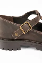 Zapato tipo guillermina de cuero lavado color marrón, con diseño de tira en T y cierre de hebilla metálica. Presenta costuras decorativas en contraste y suela de goma con plataforma dentada.