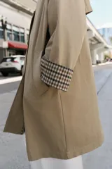 Trench de corte oversize color beige, con cuello alto, cierre frontal de botones y mangas largas con puños vueltos estampados a cuadros. Cuenta con bolsillos delanteros de vivo.