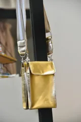 Cartera bandolera dorada de cuero sintético con correa de tela a rayas grises y blancas.