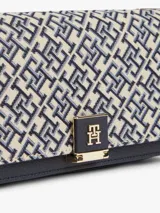 Cartera cruzada Tommy Hilfiger con diseño jacquard en tonos azul y beige, solapa con detalle de cuero sintético negro en la base y cierre con broche metálico dorado con monograma de la marca. Incluye correa de cadena dorada.