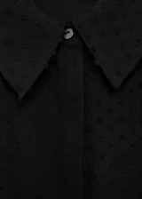 Camisa negra de tejido plumeti con cuello camisero, manga larga con puños abotonados y cierre frontal de botones ocultos.