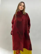 Tapado de lana merino afieltrada con diseño artesanal teñido en tonos violeta y fucsia. Presenta cuello elevado, cierre frontal con broches ocultos, bolsillos laterales y un corte ligeramente más largo en la parte trasera.