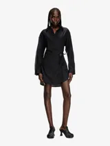Minivestido negro de corte regular con diseño de material mixto que combina popelina y denim. La parte delantera está hecha de popelina de algodón de alta densidad y la parte trasera está hecha de denim tratado. El diseño envolvente acentúa la feminidad y el charm en forma de D ovalada que cuelga de la cinta del mismo tejido es un punto icónico.