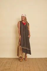 Vestido midi de lino color marrón, sin mangas y con escote en V. Presenta detalles de flecos a lo largo de la abertura y una franja bordada con lentejuelas en el ruedo. Incluye bolsillos laterales.