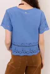 Camisa azul de manga corta confeccionada en tejido broderie con diseño calado y floral. Cuenta con escote en V y cierre frontal de botones.