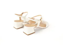 Sandalias blancas con taco de 5 cm, capellada y forro de cuero. Tienen una tira ancha en la parte delantera y una tira fina con hebilla alrededor del tobillo.
