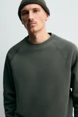 Sudadera de corte relajado confeccionada en algodón compacto con interior de rizo. Presenta cuello redondo, mangas largas tipo raglán y terminaciones en rib.