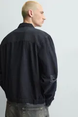 Cazadora de estilo cropped confeccionada en tejido de algodón con estructura canvas. Presenta cuello solapa, cierre frontal con cremallera y manga larga con puños abotonados. Incluye bolsillos asimétricos de plastrón en el pecho y bolsillos laterales, con un acabado de lavado efecto rotos en toda la prenda.