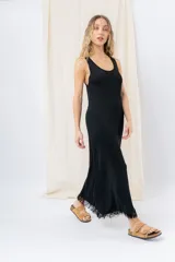 Vestido midi de tejido tipo seda con caída fluida, escote redondo y sin mangas. Presenta un diseño minimalista con detalle de flecos en el ruedo.