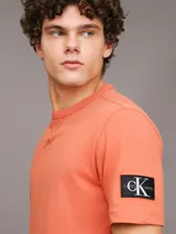 Remera color naranja de corte clásico y manga corta. Tiene cuello redondo y una insignia con el monograma de Calvin Klein en la manga.