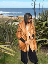 Campera oversize de abrigo color camel en tejido suave con efecto gamuzado, con gran capucha envolvente que puede usarse como bufanda, bolsillos laterales y puños elastizados negros.