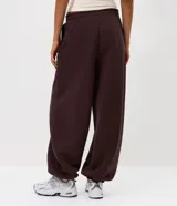 Pantalón estilo aladín de corte amplio y holgado, color marrón chocolate. Confeccionado en tejido de moletón con felpa interna, cuenta con cintura elástica y puños elásticos en los tobillos.