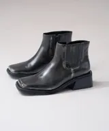Bota corta tipo chelsea de cuero vacuno color negro, con puntera cuadrada, taco cuadrado de madera y detalle de textura grabada en el panel elástico lateral.