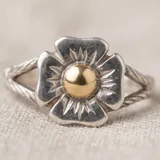 Anillo de plata con diseño de flor y detalle central dorado.